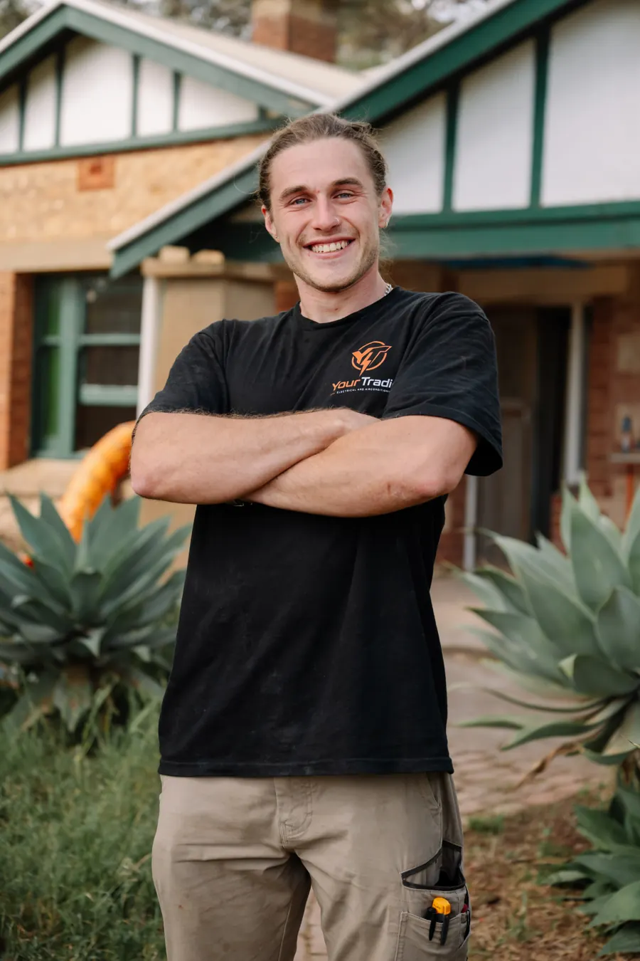 James from YourTradie, arms crossed in a branded work shirt, outside a red-brick villa